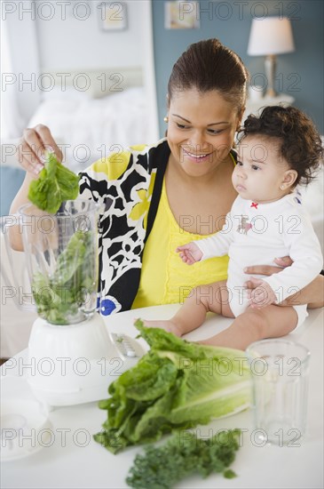 Mixed race mother holding baby and using blender