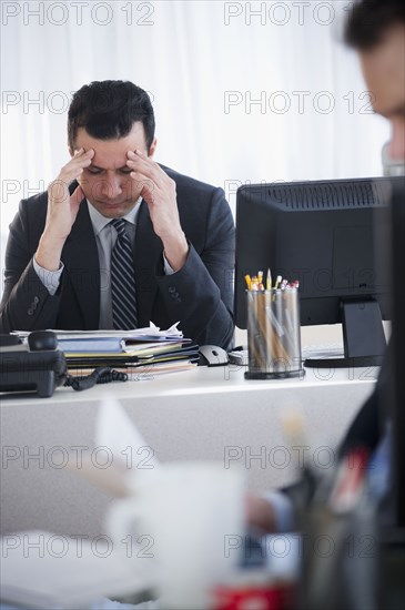 Mixed race businessman rubbing head at desk