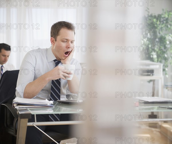Caucasian businessman drinking coffee and yawning