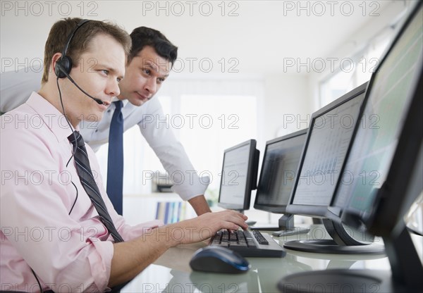 Businessmen looking at computer monitors together