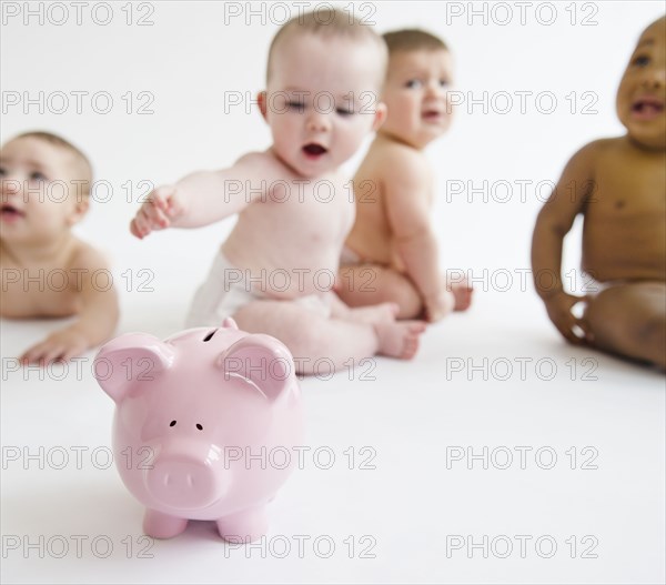 Babies sitting on floor with piggy bank