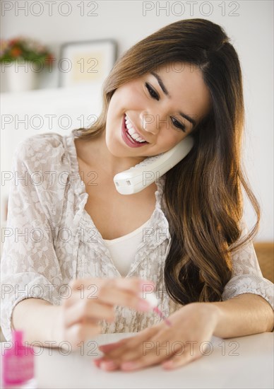 Hispanic woman talking on phone and painting fingernails