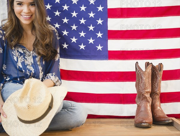 Hispanic woman holding cowboy hat and sitting next to American flag