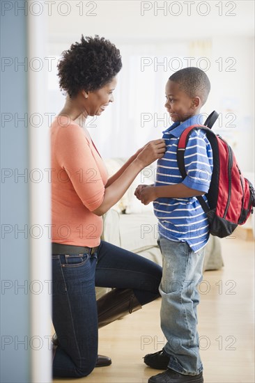 Black mother buttoning son's shirt