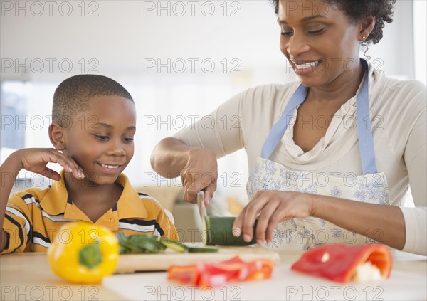 Black son watching mother slicing vegetables