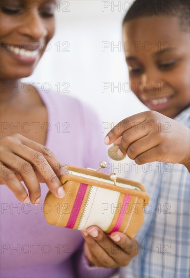 Black son putting coins into mother's purse