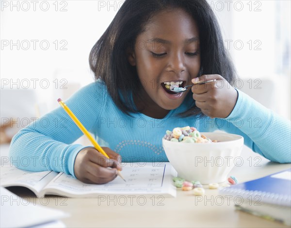 Black girl eating cereal and writing in workbook