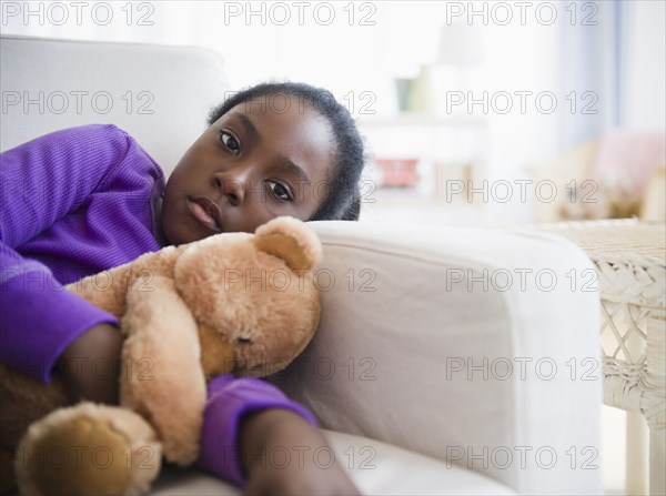 Black girl laying on sofa with teddy bear