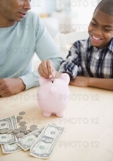 Father watching son put coin in piggy bank