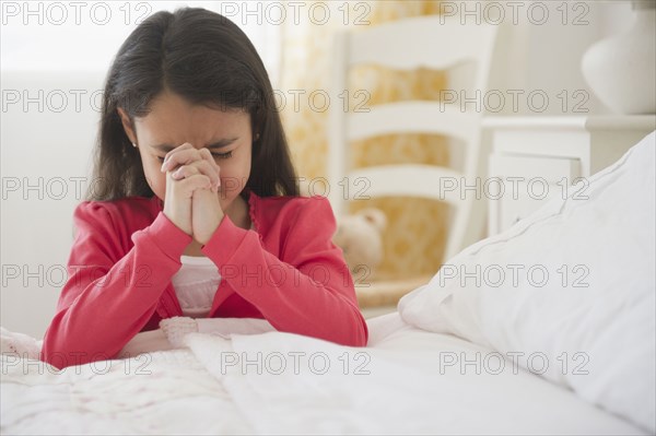 Mixed race girl praying in bedroom
