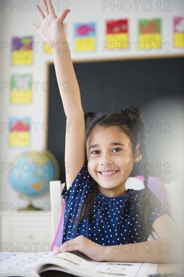 Mixed race girl raising her hand in classroom