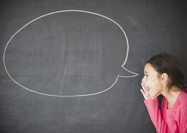 Mixed race girl standing by speech bubble on blackboard