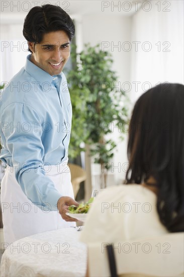 Mixed race waiter serving woman salad