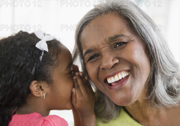 African American girl telling secret to grandmother