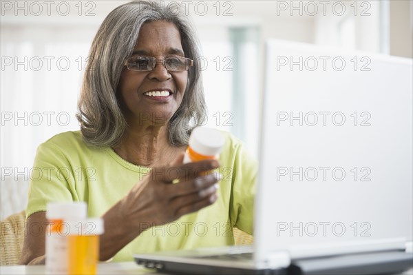 African American woman holding pill bottle and using laptop