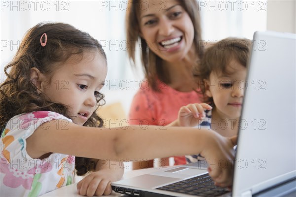 Mother watching children using laptop