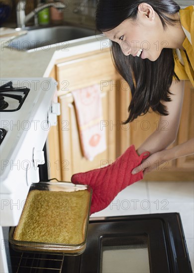 Asian woman taking cake from oven