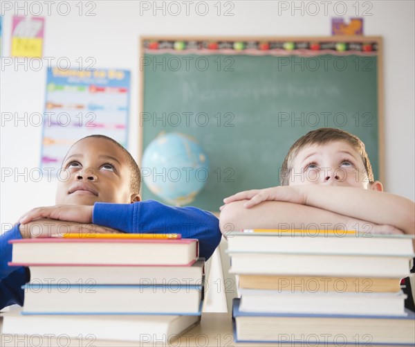 Students leaning on stacks of books in classroom