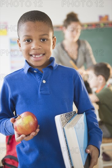 African American boy holding apple in classroom