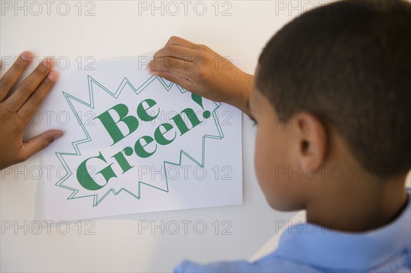 Hispanic boy putting up be green sign