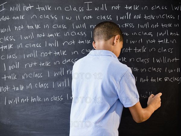 Hispanic boy writing punishment on blackboard