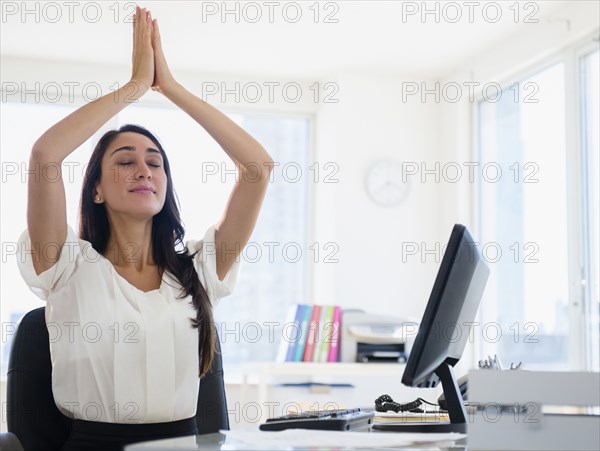 Caucasian businesswoman meditating at desk