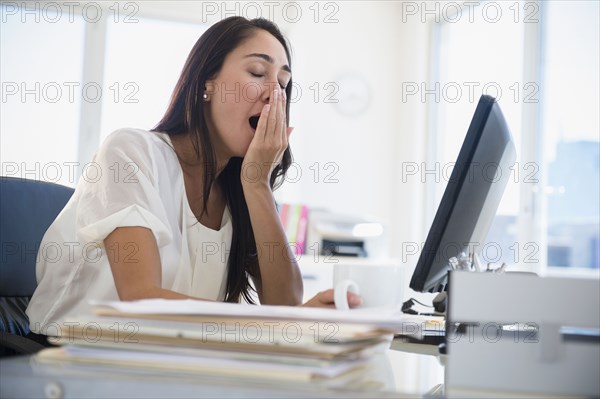 Caucasian businesswoman yawning at desk