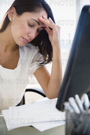 Caucasian businesswoman rubbing forehead at desk