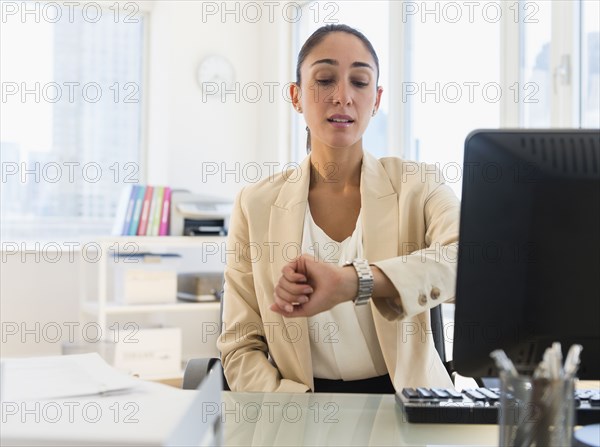 Caucasian businesswoman checking watch at desk