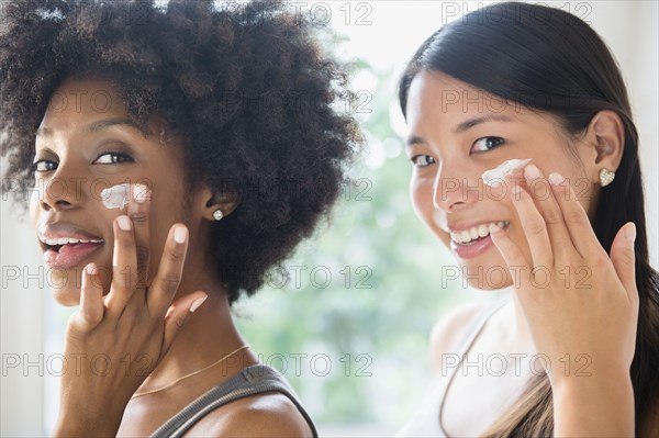 Smiling women applying moisturizer to cheeks