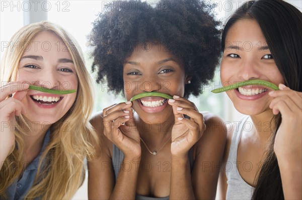 Smiling women using green beans as mustaches