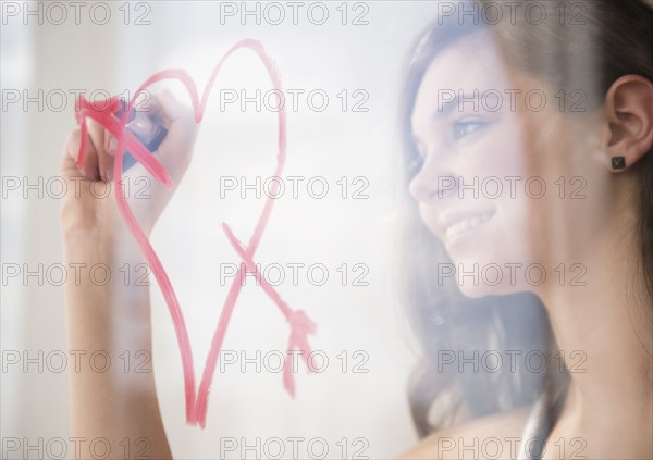 Hispanic girl drawing heart with arrow on window