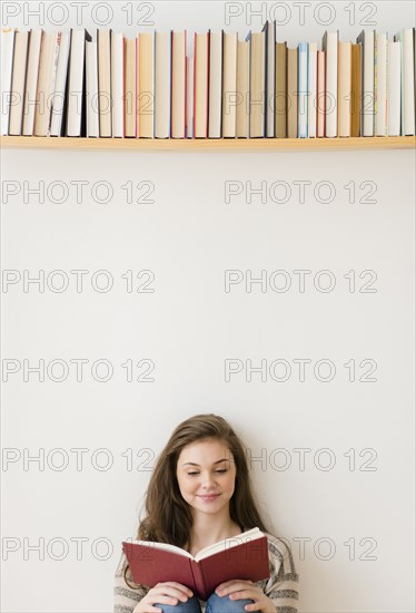 Hispanic girl reading under bookshelf