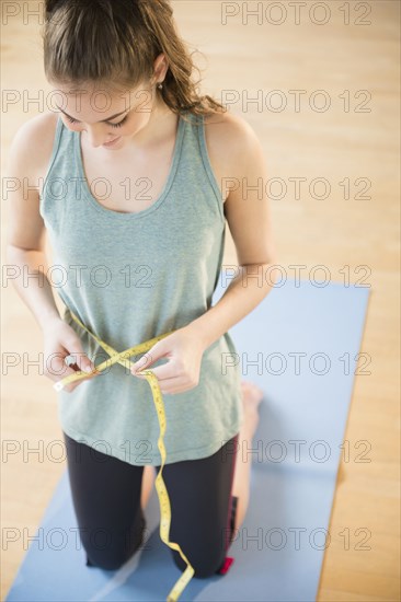 Hispanic girl measuring her waist on yoga mat