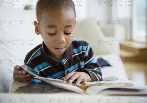 African American boy reading book on sofa