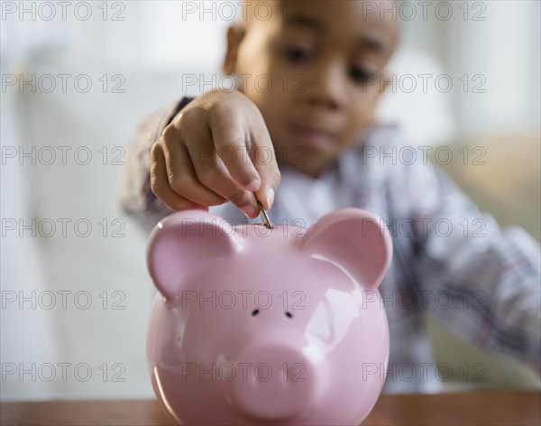 African American boy putting coins in piggy bank