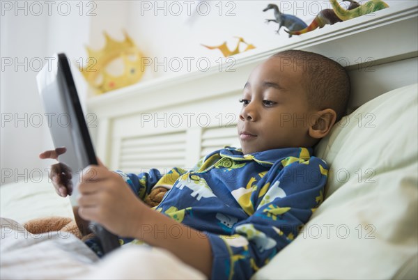 African American boy using tablet computer in bed