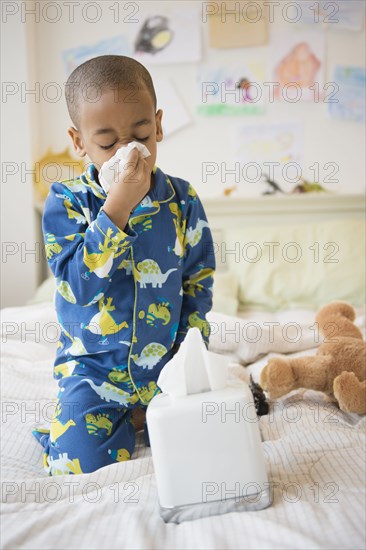 African American boy blowing his nose on bed