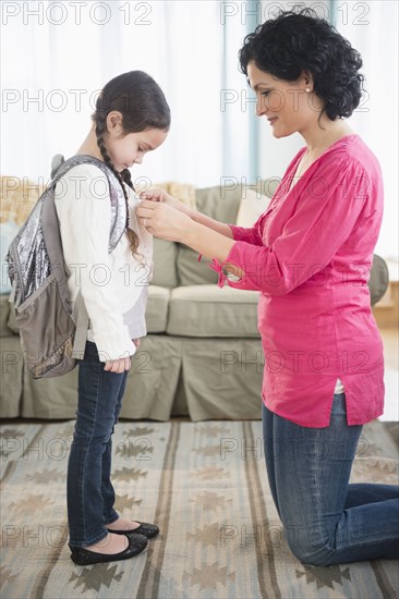 Mother buttoning daughter's sweater in living room