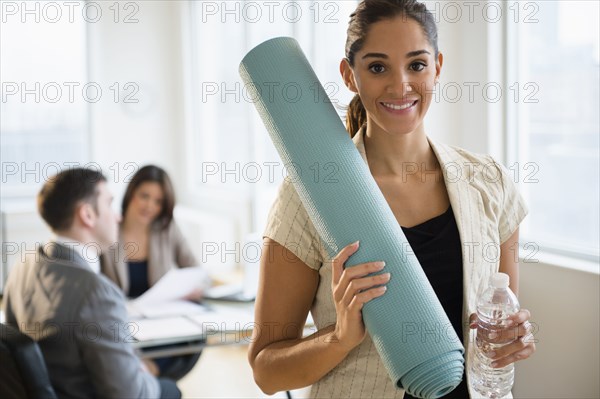 Businesswoman holding yoga mat in office