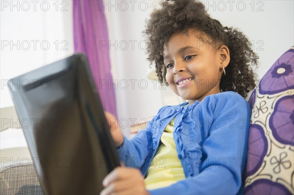 African American girl using tablet computer on sofa
