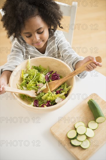 African American girl tossing salad at table