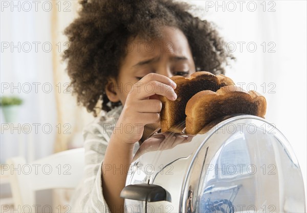 African American girl burning toast in toaster