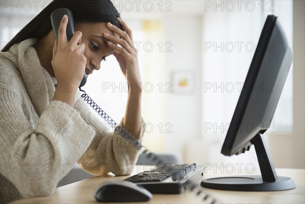 Mixed race woman talking on phone at desk