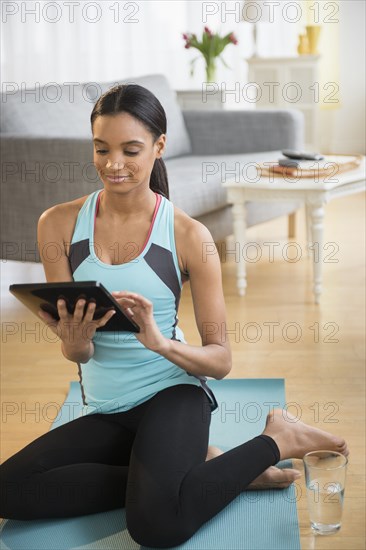 Mixed race woman using tablet computer on yoga mat