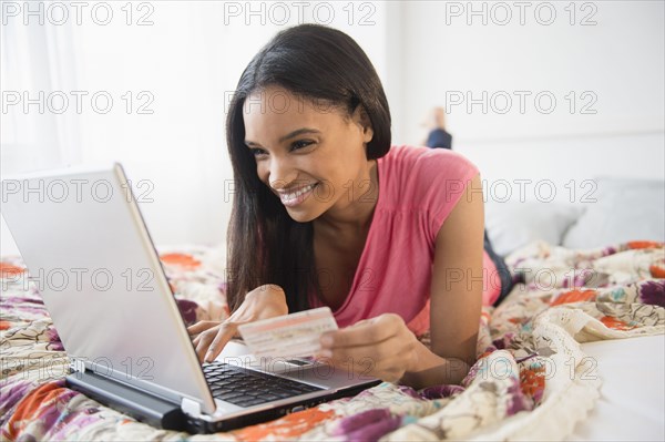 Mixed race woman using laptop on bed