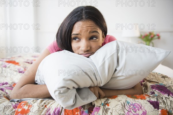 Mixed race woman hugging pillow on bed