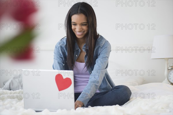 Mixed race woman using laptop on bed