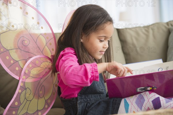 Hispanic girl wearing fairy wings on sofa