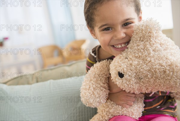 Hispanic girl hugging teddy bear on sofa